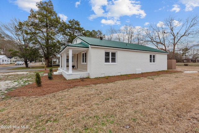 view of home's exterior with metal roof, covered porch, brick siding, crawl space, and a lawn