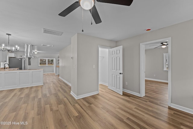 unfurnished living room featuring light wood-style floors, visible vents, a sink, and baseboards