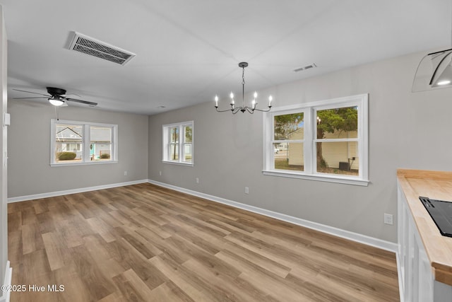 unfurnished dining area with baseboards, ceiling fan with notable chandelier, visible vents, and light wood-style floors