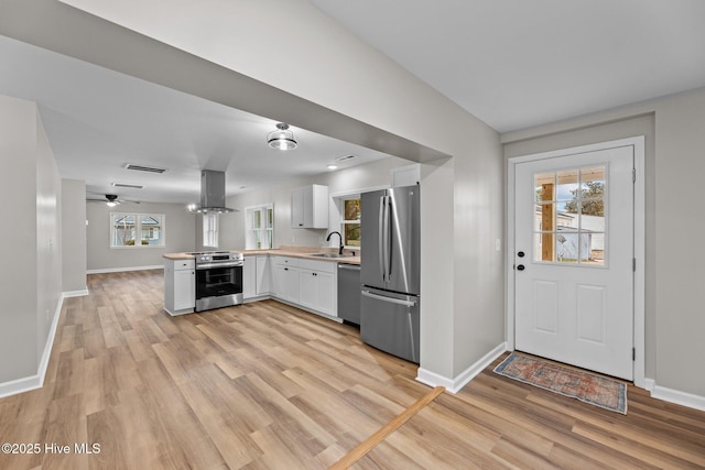 kitchen featuring island exhaust hood, stainless steel appliances, light countertops, white cabinetry, and a sink