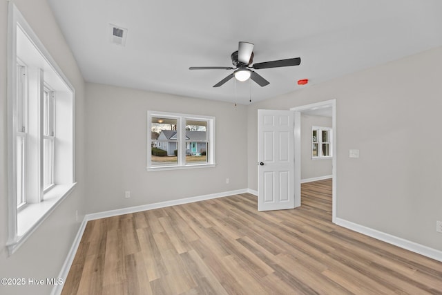 empty room featuring light wood finished floors, baseboards, visible vents, and a ceiling fan