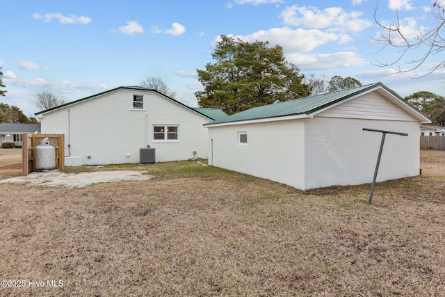 back of house with central AC unit, metal roof, and a lawn