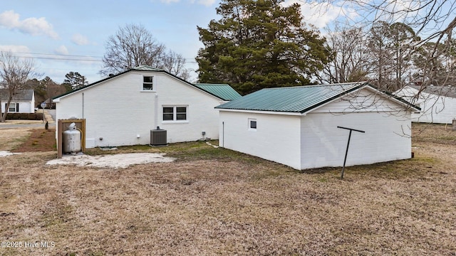 back of house with brick siding, metal roof, central AC, and a yard