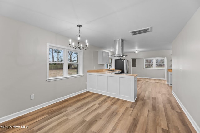 kitchen with visible vents, pendant lighting, a peninsula, island exhaust hood, and wooden counters