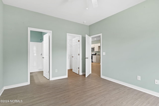 unfurnished bedroom featuring a walk in closet, wood-type flooring, ensuite bath, and a closet