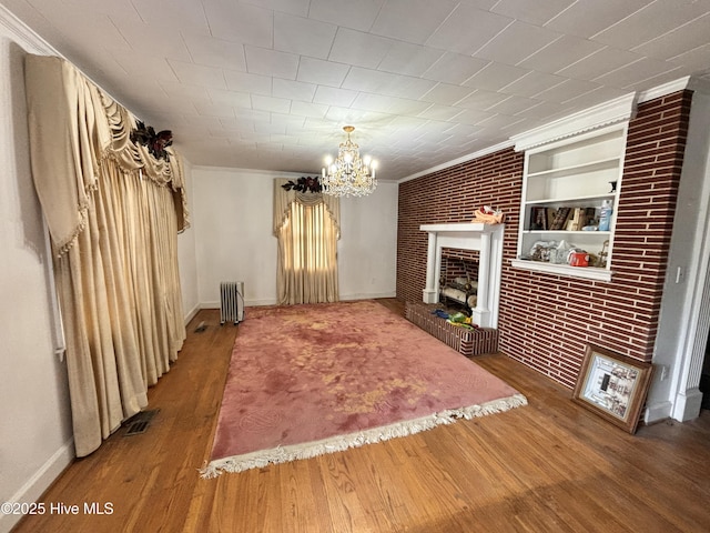 unfurnished living room featuring brick wall, radiator heating unit, a brick fireplace, and wood finished floors