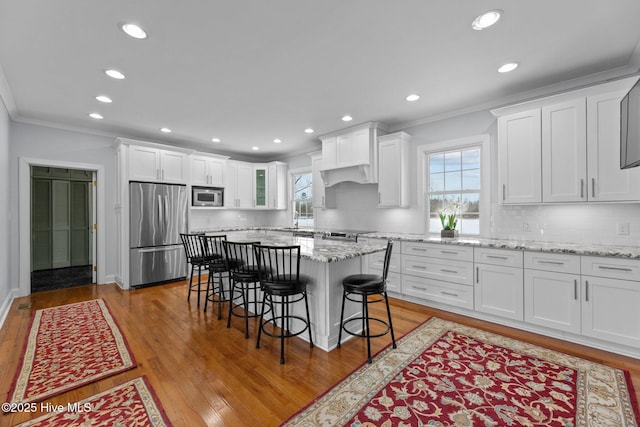 kitchen featuring a kitchen island, a breakfast bar area, white cabinets, stainless steel appliances, and light stone countertops