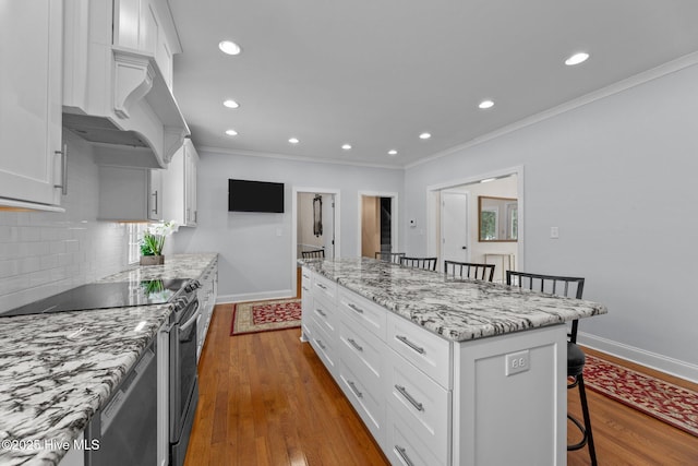 kitchen with a breakfast bar, a center island, electric range, light stone countertops, and white cabinets