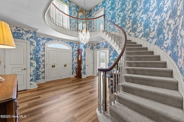 entryway with an inviting chandelier, a towering ceiling, wood-type flooring, and plenty of natural light