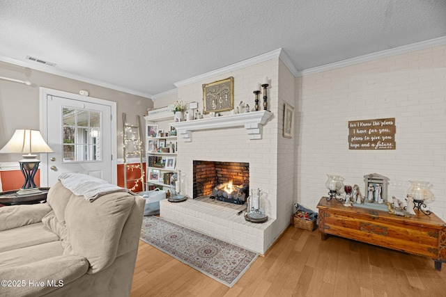 living room featuring ornamental molding, a textured ceiling, a brick fireplace, and light wood-type flooring