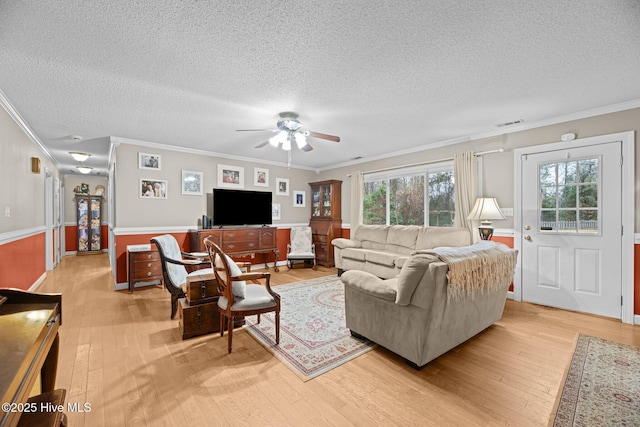 living room with ceiling fan, ornamental molding, a textured ceiling, and light wood-type flooring