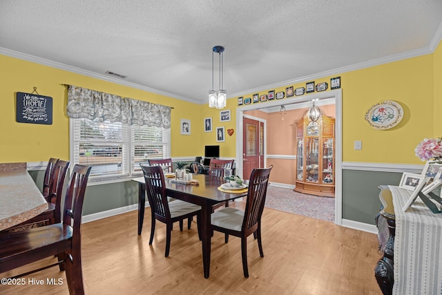 dining space with crown molding, a textured ceiling, and light hardwood / wood-style flooring