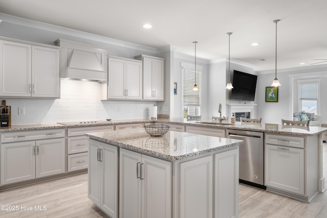 kitchen featuring sink, dishwasher, premium range hood, hanging light fixtures, and a center island