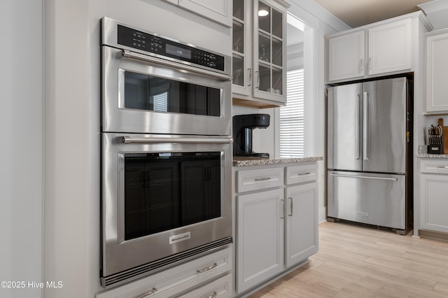 kitchen with light stone counters, appliances with stainless steel finishes, light hardwood / wood-style floors, and white cabinets