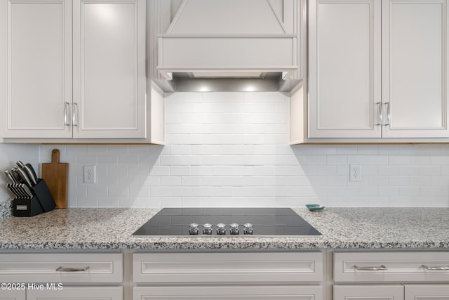 kitchen with backsplash, light stone counters, custom range hood, white cabinets, and black electric cooktop