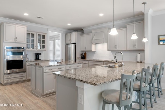 kitchen with appliances with stainless steel finishes, a peninsula, hanging light fixtures, custom exhaust hood, and a sink