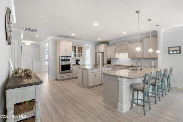 kitchen featuring sink, a breakfast bar area, appliances with stainless steel finishes, hanging light fixtures, and an island with sink