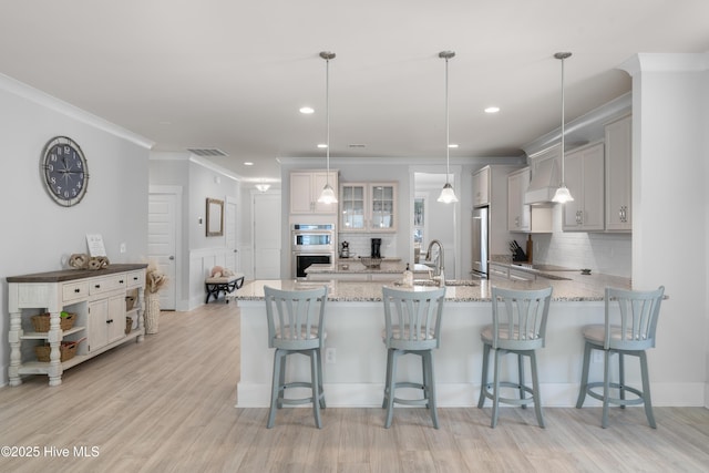 kitchen featuring a breakfast bar area, a sink, hanging light fixtures, appliances with stainless steel finishes, and glass insert cabinets