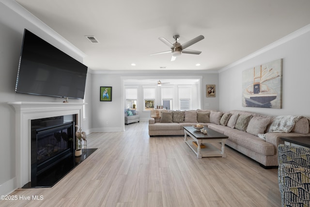 living room with light wood-style flooring, visible vents, baseboards, ornamental molding, and a glass covered fireplace