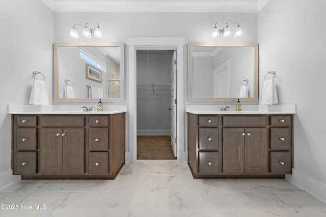 bathroom with a walk in closet, marble finish floor, two vanities, and baseboards