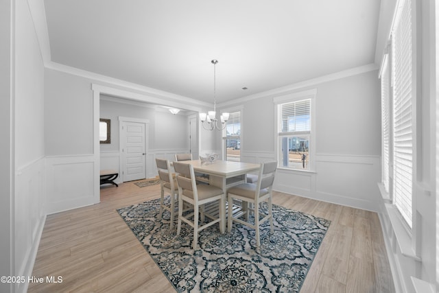 dining room with light wood-style flooring, crown molding, and wainscoting