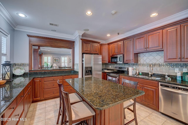 kitchen with appliances with stainless steel finishes, sink, a kitchen bar, dark stone counters, and a center island