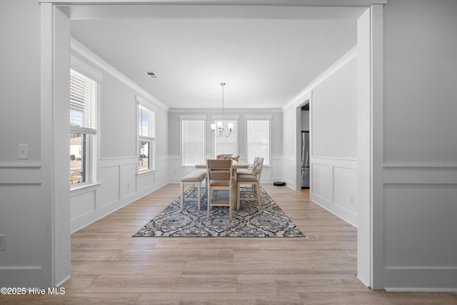 dining area featuring a chandelier, light wood finished floors, ornamental molding, and visible vents