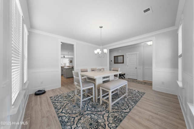 dining area with ornamental molding, light wood finished floors, a chandelier, and visible vents