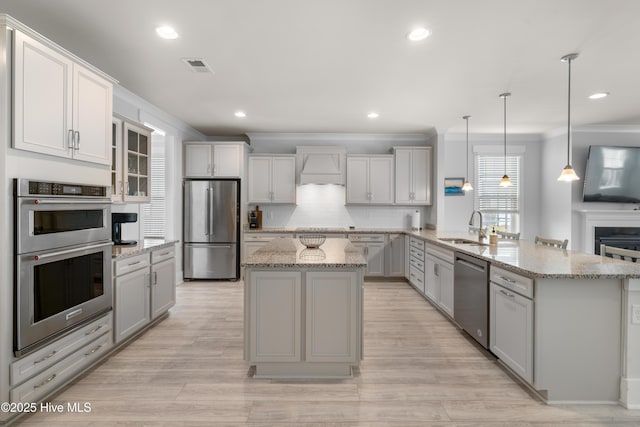 kitchen featuring a kitchen island with sink, decorative light fixtures, a sink, appliances with stainless steel finishes, and glass insert cabinets