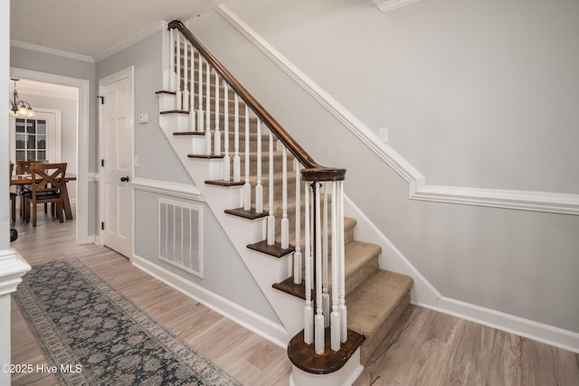 staircase with hardwood / wood-style floors, crown molding, and a notable chandelier