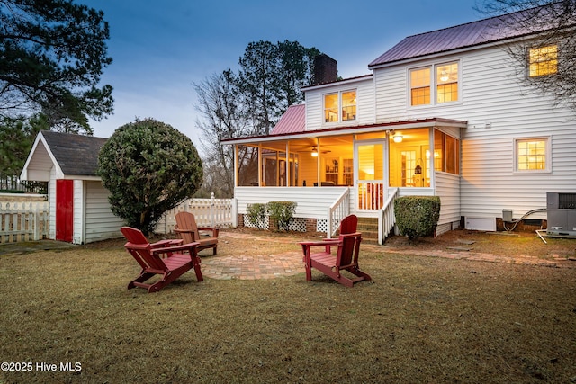 back house at dusk featuring a lawn, central AC unit, ceiling fan, a sunroom, and a patio area