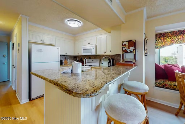 kitchen with a breakfast bar, kitchen peninsula, white cabinets, white appliances, and backsplash