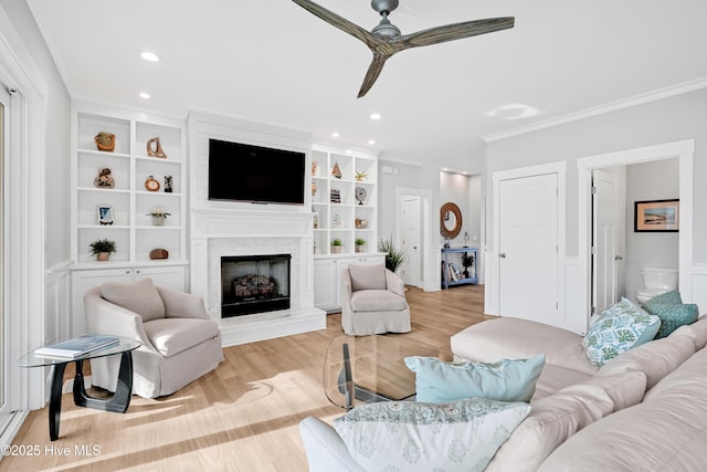 living area featuring light wood-type flooring, recessed lighting, ceiling fan, a fireplace, and ornamental molding