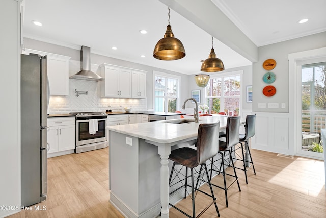 kitchen featuring wall chimney exhaust hood, stainless steel appliances, a sink, light wood-type flooring, and white cabinetry