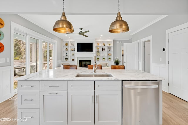 kitchen featuring stainless steel dishwasher, a sink, open floor plan, ceiling fan, and a fireplace