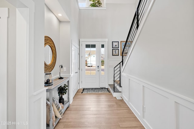 foyer entrance with wainscoting, light wood-style floors, a high ceiling, stairs, and a decorative wall