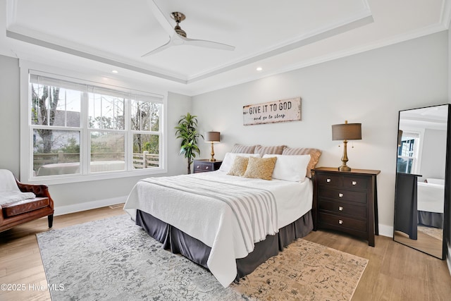 bedroom featuring a raised ceiling, light wood-style flooring, ornamental molding, baseboards, and ceiling fan