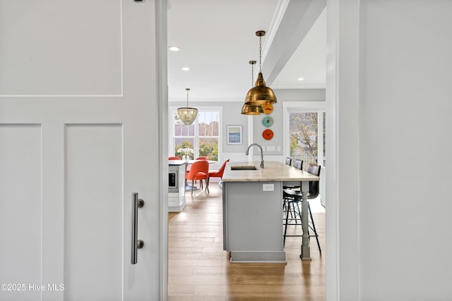 kitchen with ornamental molding, a sink, light wood-style floors, a center island with sink, and a breakfast bar area