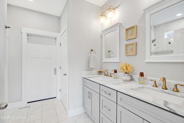 full bathroom with a tile shower, double vanity, marble finish floor, and a sink