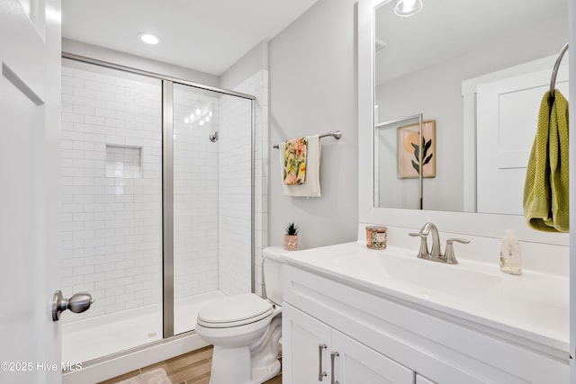 bathroom with recessed lighting, wood finished floors, toilet, vanity, and a stall shower