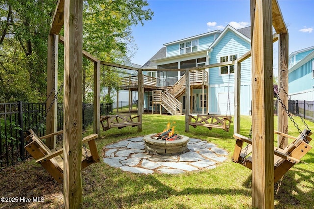 rear view of house with stairs, a fenced backyard, a yard, an outdoor fire pit, and a sunroom