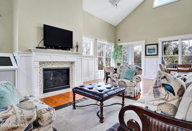 living room with light wood-style flooring, a wealth of natural light, a decorative wall, a stone fireplace, and high vaulted ceiling