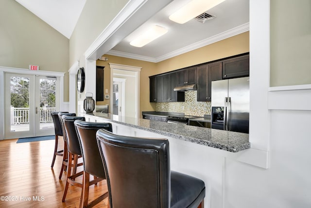 kitchen featuring light wood finished floors, tasteful backsplash, crown molding, a breakfast bar, and appliances with stainless steel finishes