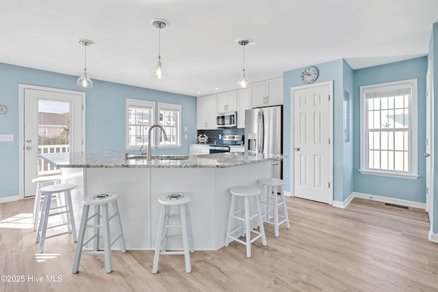 kitchen with sink, appliances with stainless steel finishes, white cabinetry, hanging light fixtures, and light stone countertops