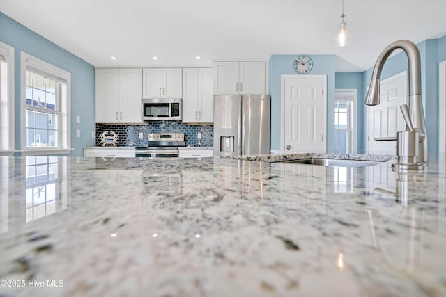 kitchen featuring decorative light fixtures, appliances with stainless steel finishes, light stone countertops, decorative backsplash, and white cabinets