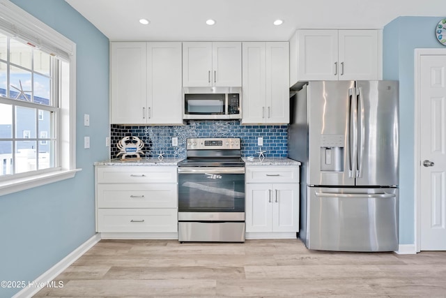 kitchen with stainless steel appliances, white cabinetry, light stone countertops, and decorative backsplash