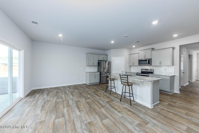 kitchen with gray cabinets, an island with sink, appliances with stainless steel finishes, and a kitchen bar