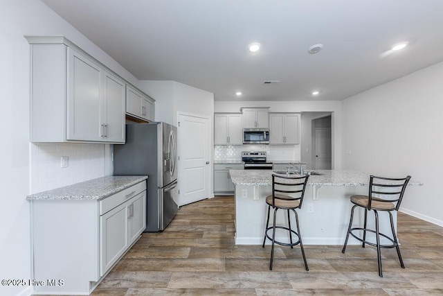 kitchen featuring stainless steel appliances, a kitchen breakfast bar, light stone countertops, and a center island with sink