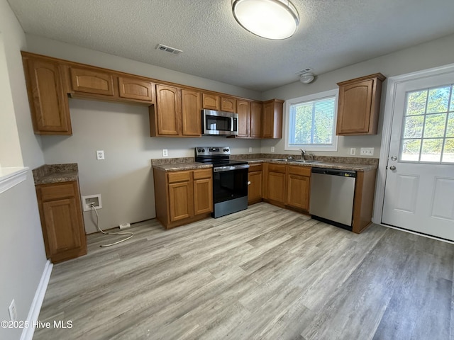 kitchen with stainless steel appliances, sink, a textured ceiling, and light wood-type flooring