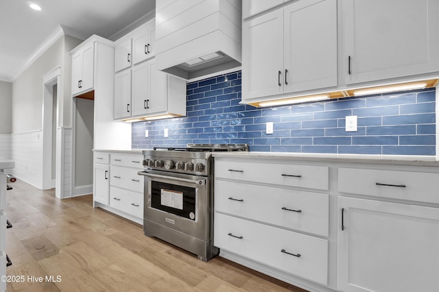 kitchen with crown molding, premium range hood, stainless steel gas stove, white cabinets, and light wood-type flooring